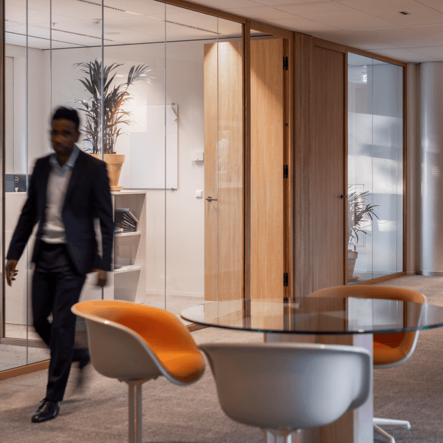 Man in suit walking past meeting rooms with glass walls HVK Stevens