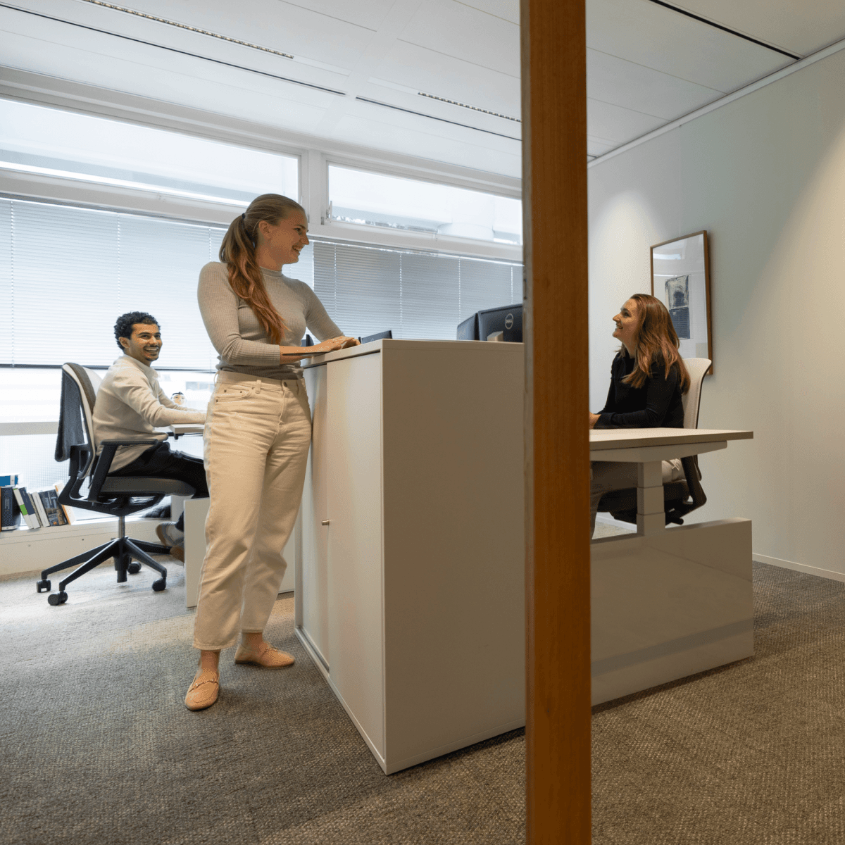 drie collega’s lachend en overleggend in lichte kantoorruimte hvk stevens