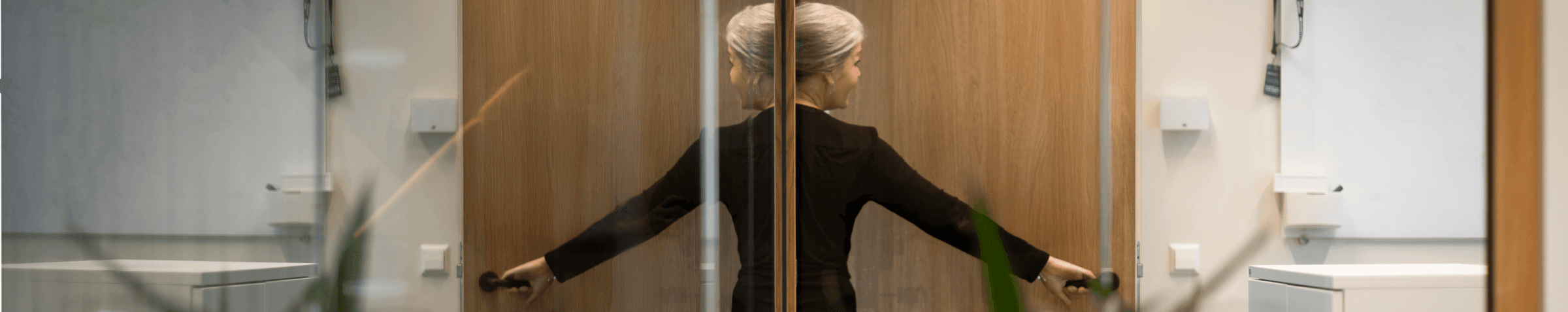 vrouw opent houten deur in modern kantoor met planten hvk stevens