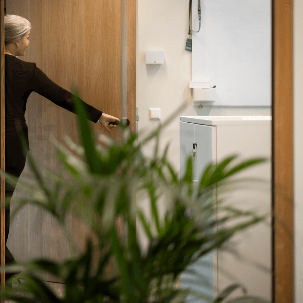 Vrouw opent houten deur in modern kantoor met planten HVK Stevens