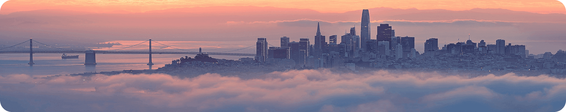 San Francisco skyline with Bay Bridge at sunrise above fog