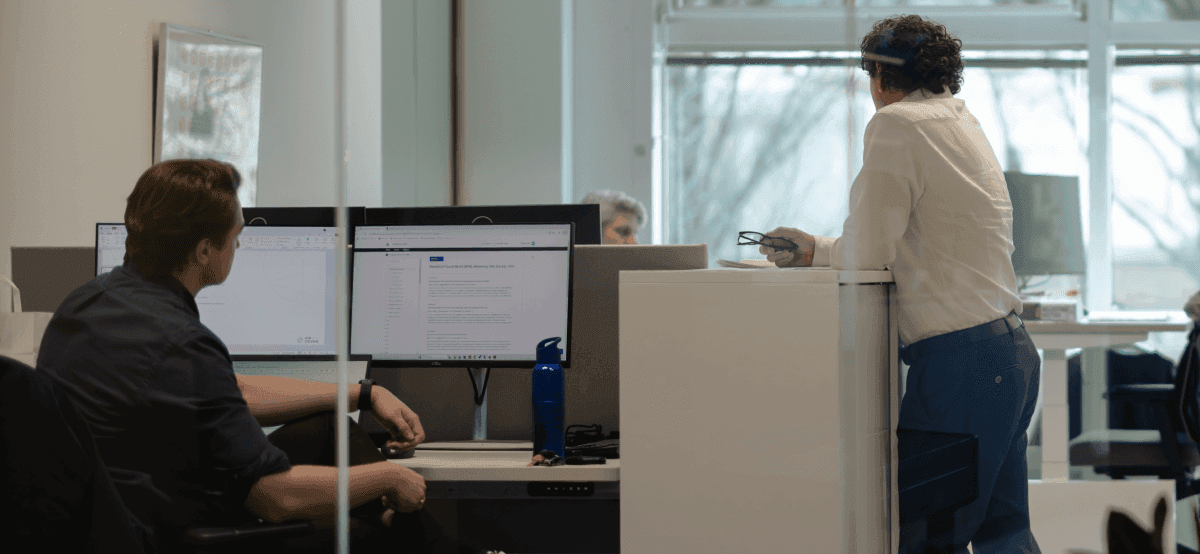 Twee collega’s in overleg bij werkplek met computerschermen